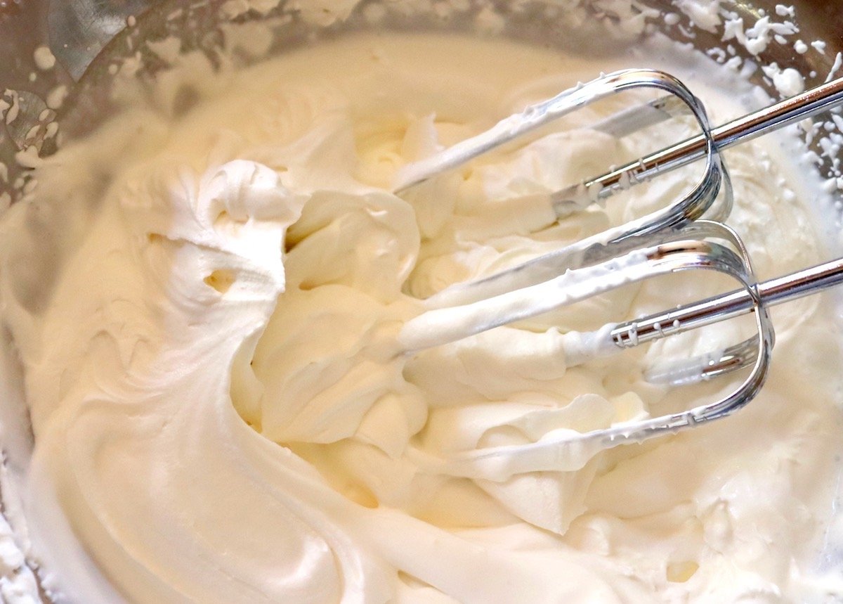 Bowl with whipped cream and electric mixer beaters.