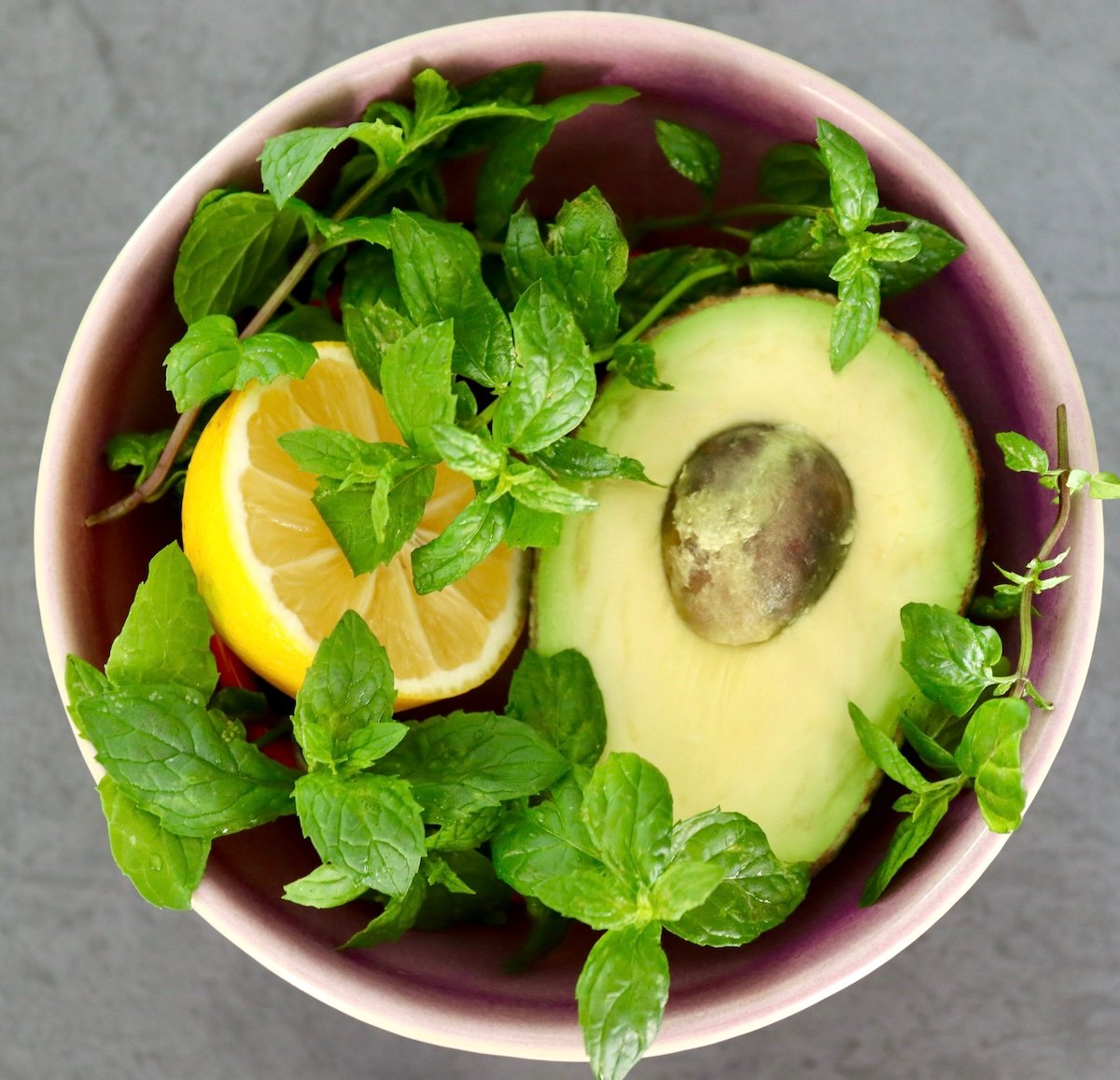 Purple ceramic bowl wotj half an avocado, half a lemon and lots of fresh mint.