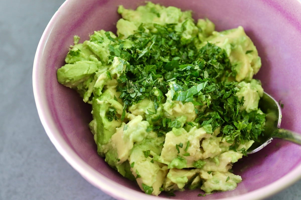 Chunks of avocado and chopped fresh mint in a purple bowl with a spoon.