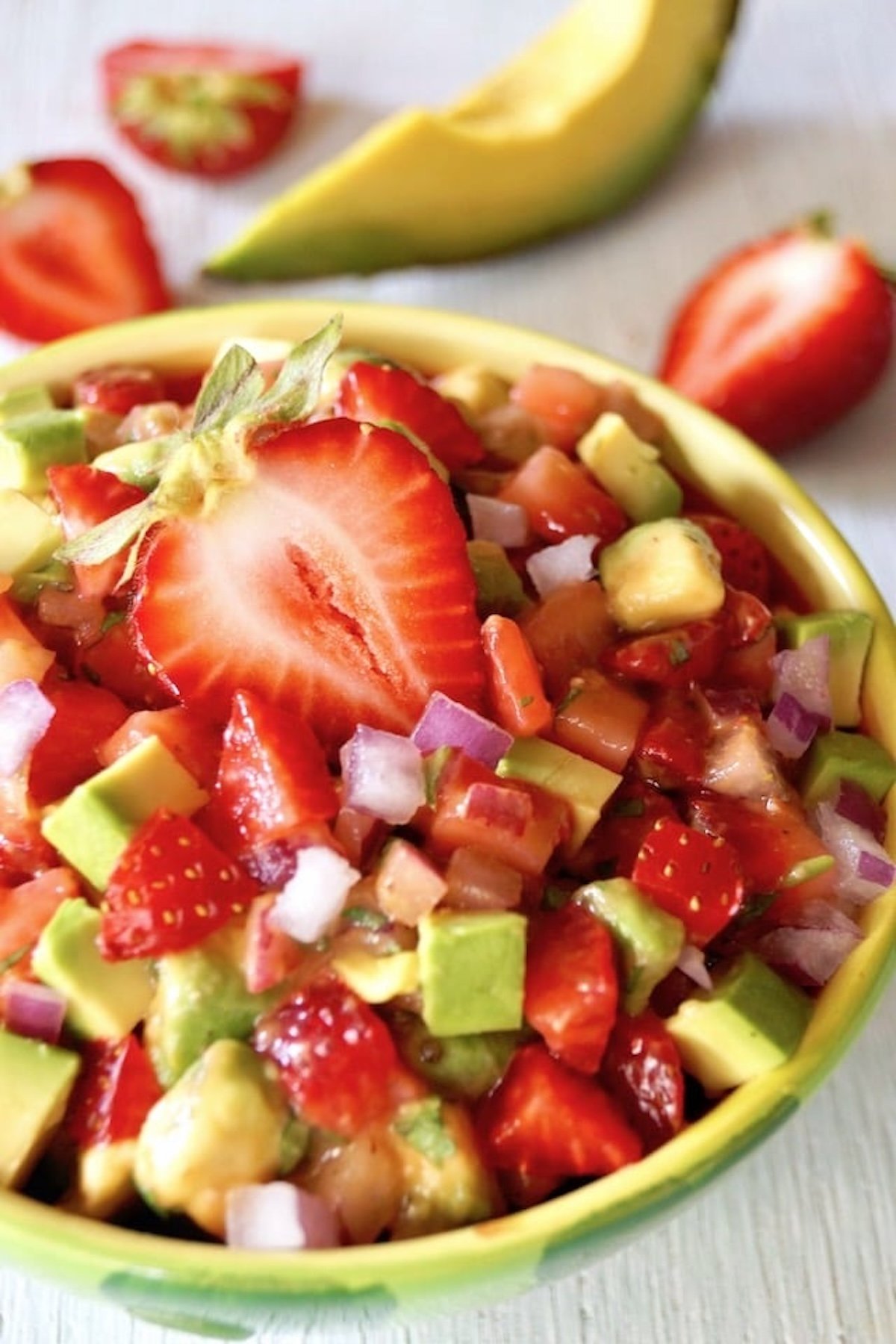 Strawberry-Avocado-Salsa-Recipe Light green bowl filled with strawberry and avocado salsa, with a halved strawberry on top.