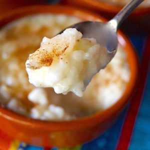 Arroz con Leche in teracotta ramekin with one bite held in the air in spoon.