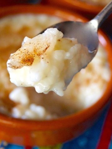 Arroz con Leche in teracotta ramekin with one bite held in the air in spoon.