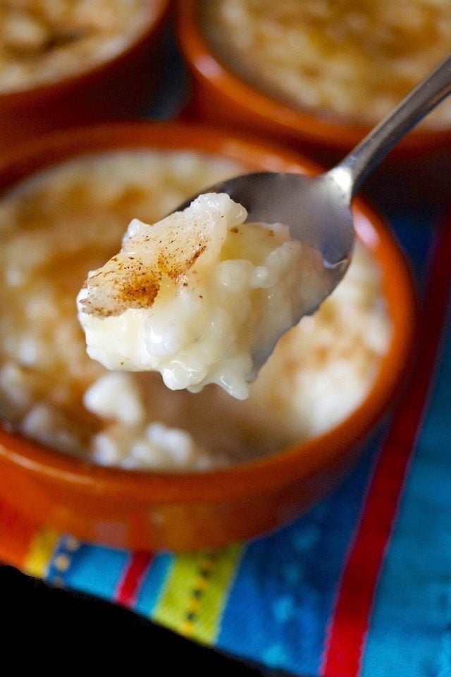 Arroz con Leche in terra cotta ramekin with one bite held in the air in spoon