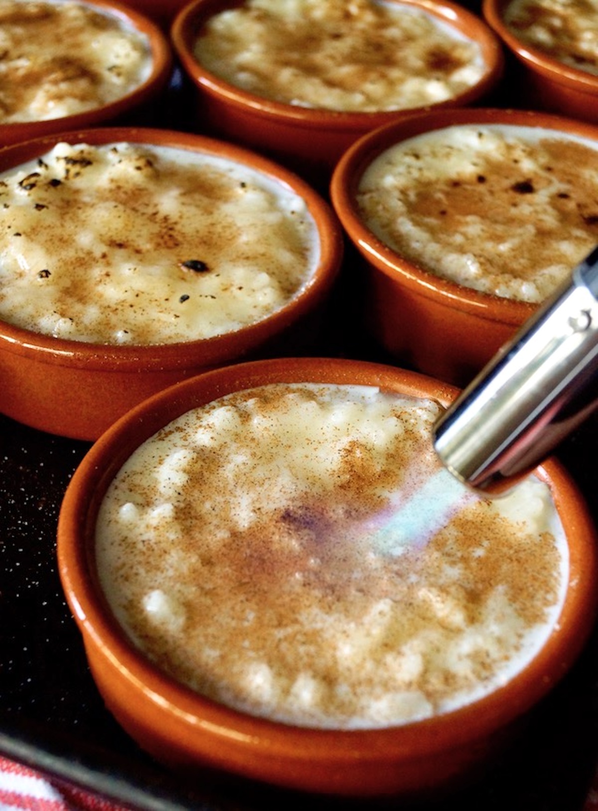 How-to-Make-Rice-Pudding Several terra cotta ramekins with rice pudding, with a kitchen blow torch being used to brulee them.
