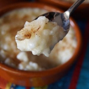 Arroz con Leche in teracotta ramekin with one bite held in the air in spoon