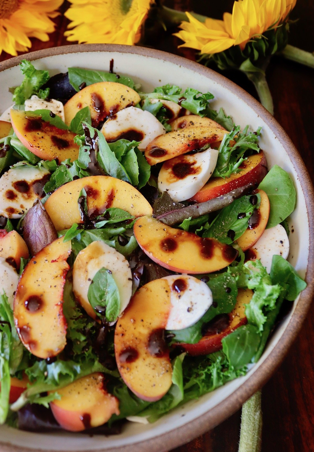 Cream-colored ceramic bowl filled to the top with Peach Caprese Salad with drops of balsamic glaze.