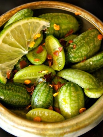 Close up of halved cucamelons in a tiny ceramic bowl with chile flakes.