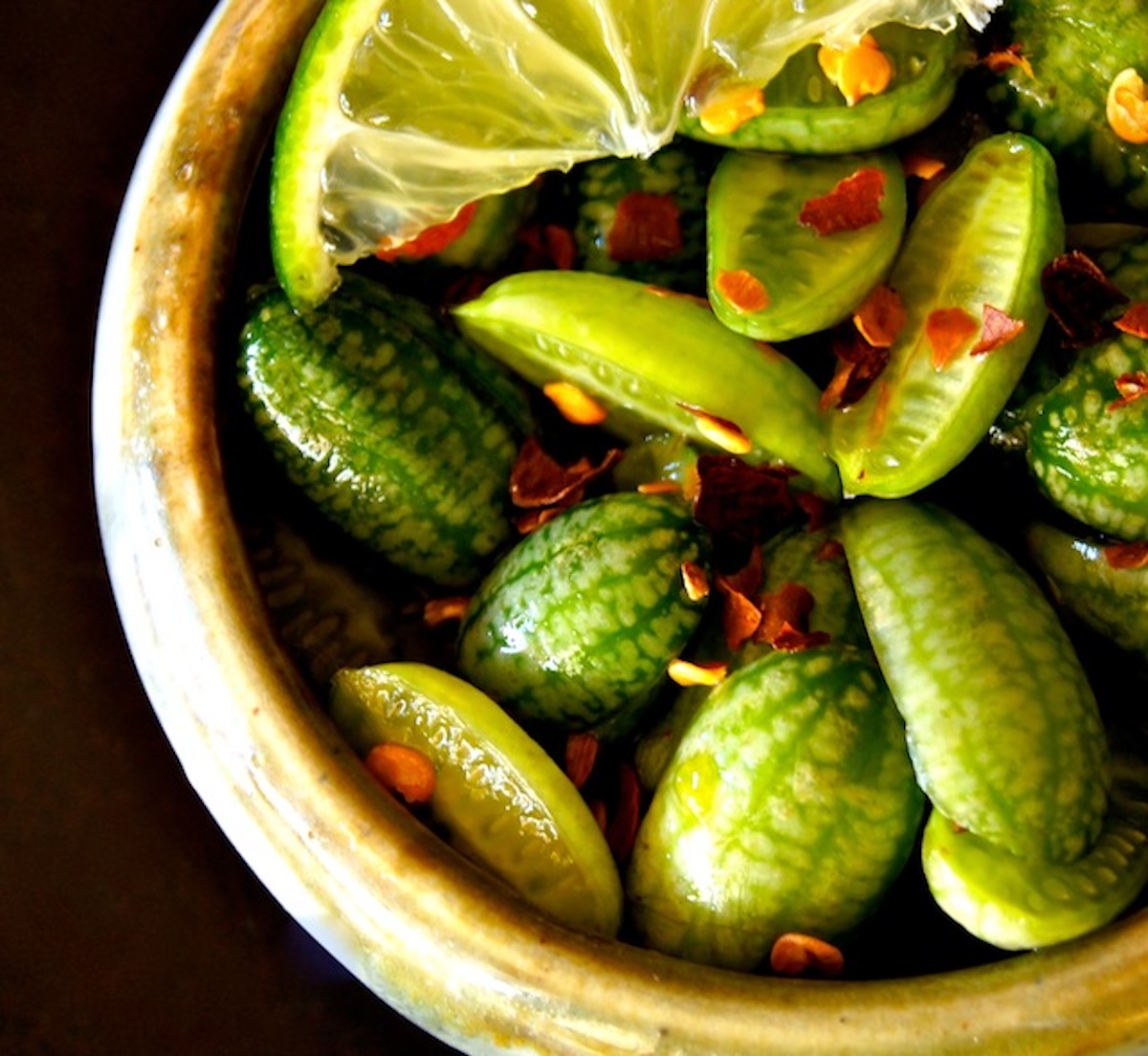 Ponzu-Marinated-Cucamelon-Recipe Close up of halved cucamelons in a tiny ceramic bowl with chile flakes.