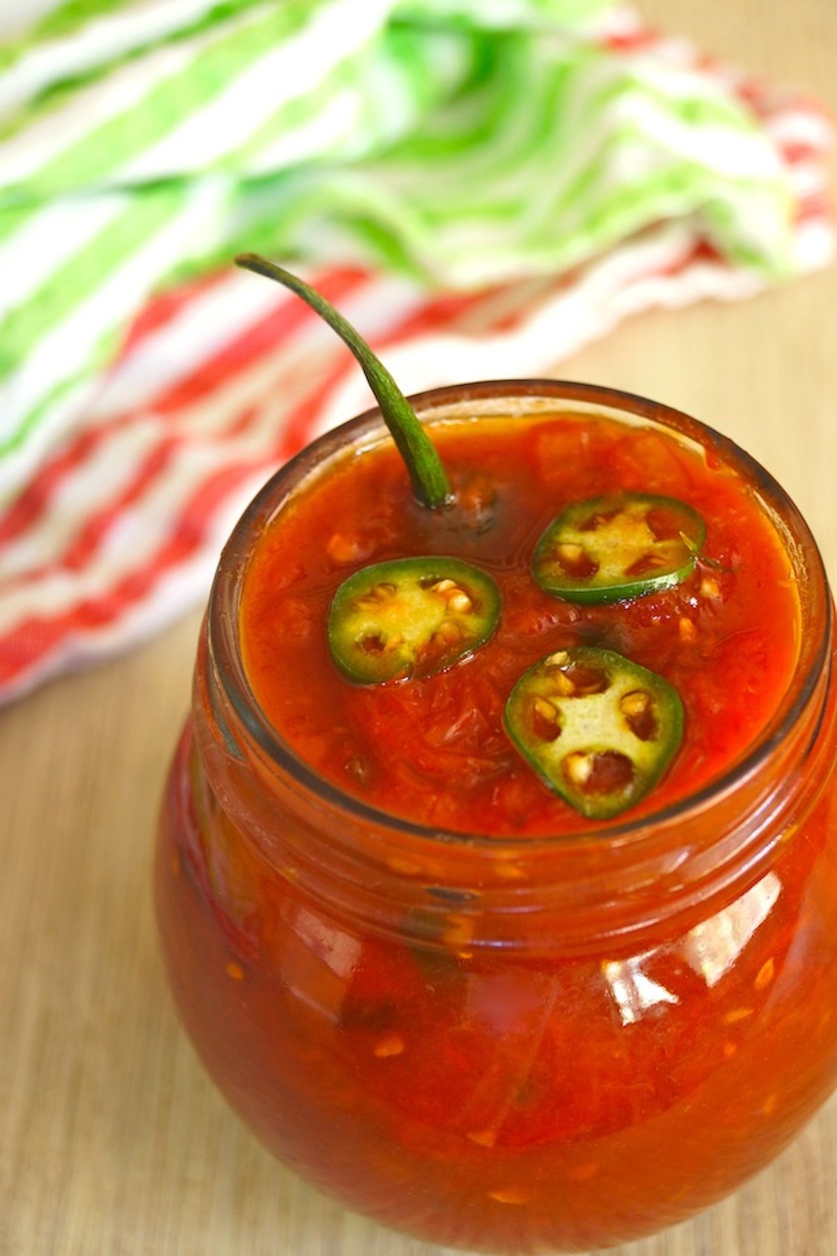 Tomato-Preserves Spicy Serrano-Tomato Preservesin a round jar with serrano stem poking out.