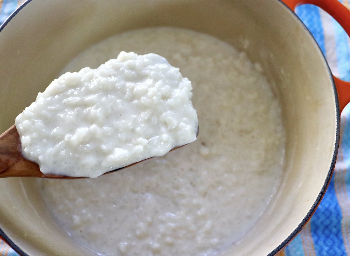 Wooden spatula holding up super creamy arroz con leche (rice pudding).