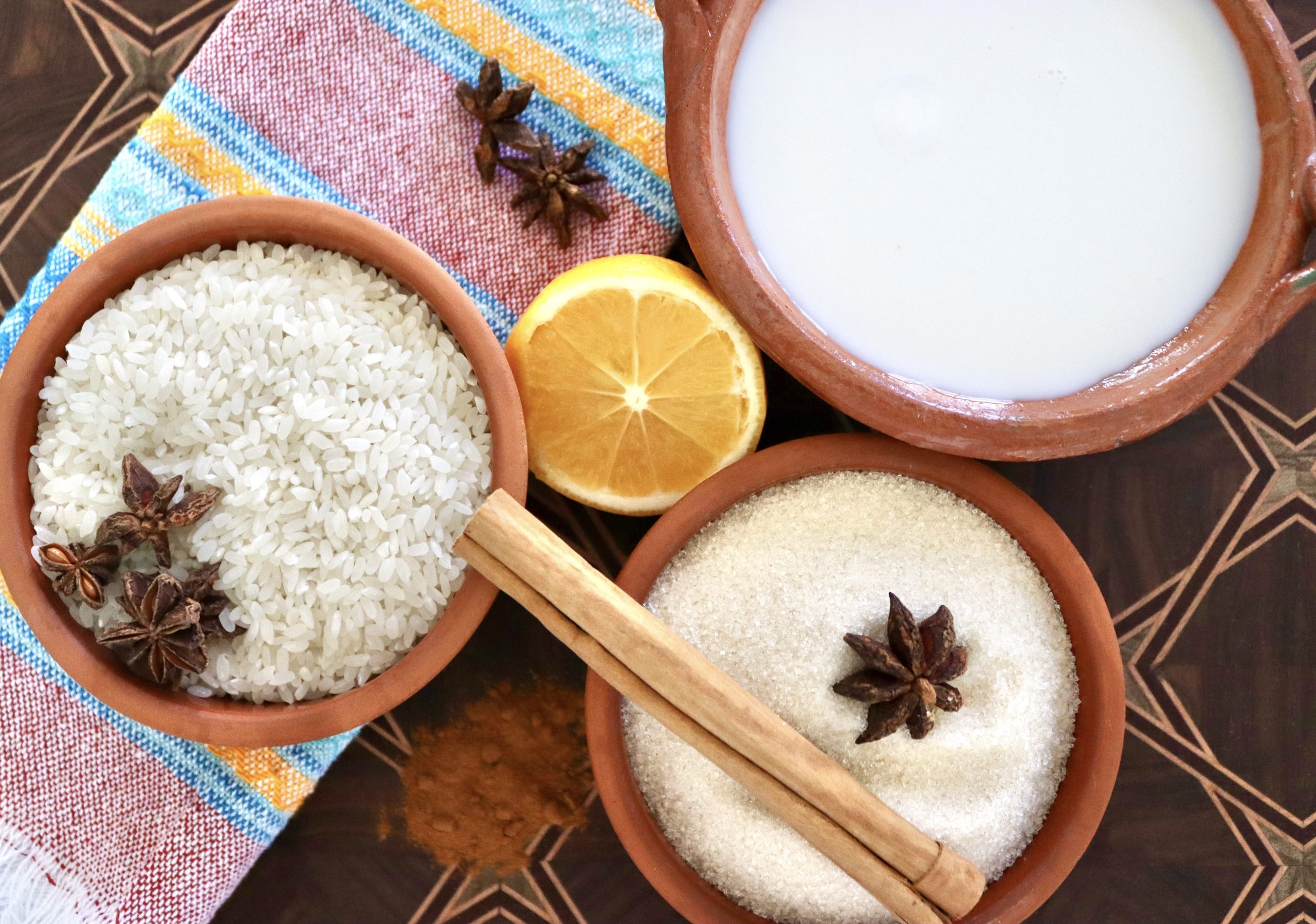How-to-Make-Rice-Pudding Ingredients for arroz con leche including rice, lemon, cinnamon stick, star anise, sugar and milk - all in terra cotta ramekins.