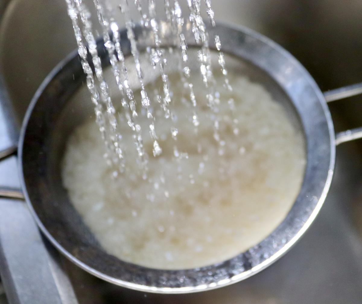 How-to-Make-Rice-Pudding Rice being rinsed with water in a colander.