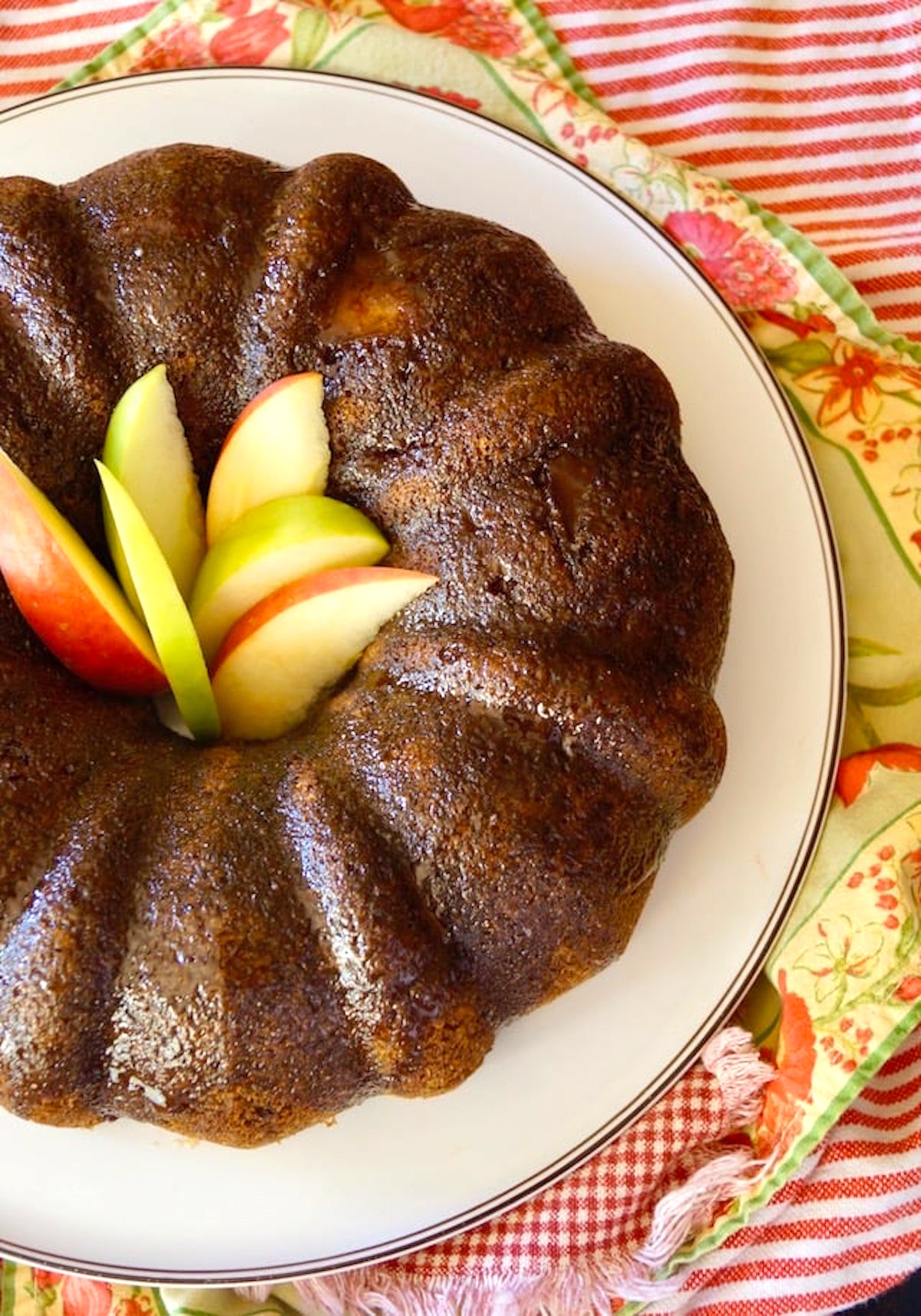 Top view of Bundt Chai Cake on a white platter with green and red apple slices in the middle.