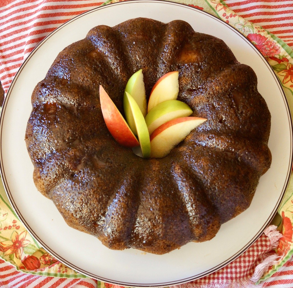 Top view of Bundt Chai Cake on a white platter with green and red apple slices in the middle.