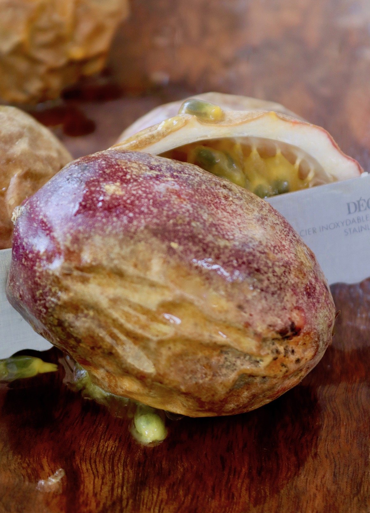 Serrated knife slicing wrinkled passion fruit.