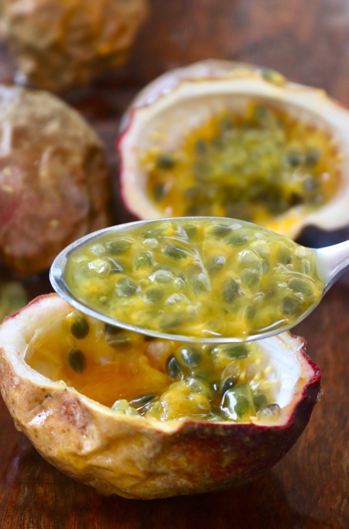 Spoonfull of passions fruit pulp over its skin on cutting board.