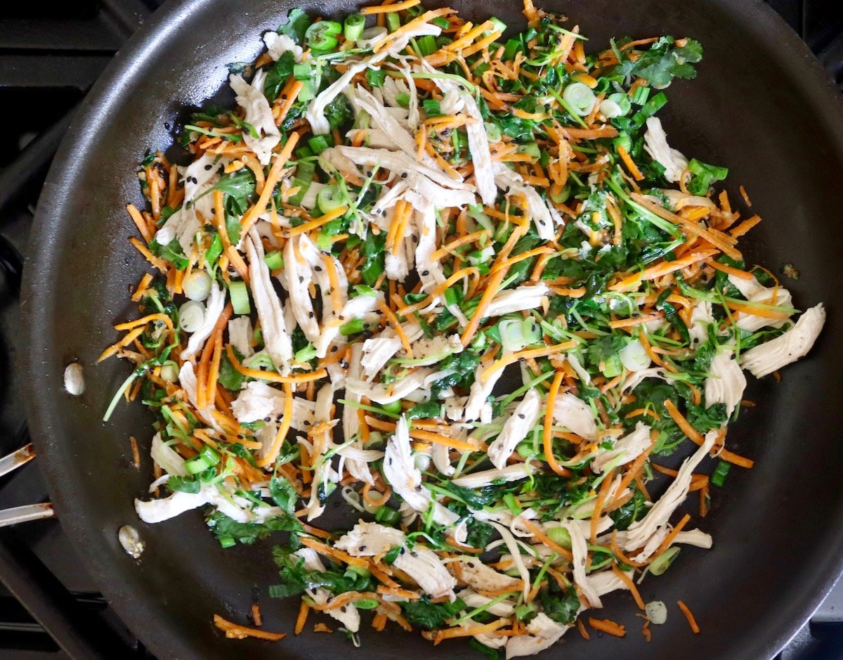 Large saute pan with greens, shredded chicken and carrots.
