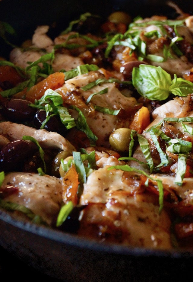 Skillet Chicken Thighs with Apricots and Oilves in cast iron pan with basil on top