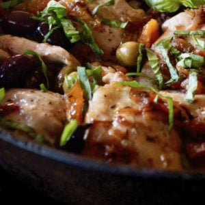 Close up of Skillet Chicken Thighs with Apricots and Oilves in cast iron pan with basil