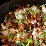 Top view of Skillet Chicken Thighs with Apricots and Oilves in cast iron pan with fresh basil
