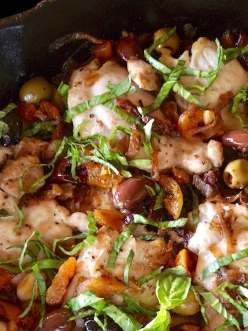 Top view of Skillet Chicken Thighs with Apricots and Oilves in cast iron pan with fresh basil