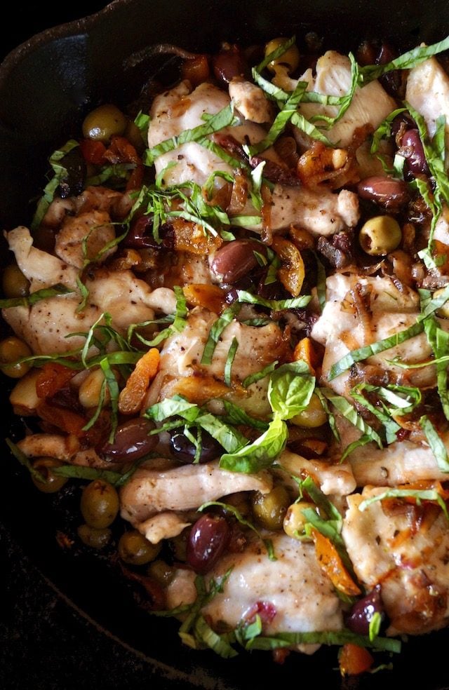 Top view of Skillet Chicken Thighs with Apricots and Oilves in cast iron pan with fresh basil