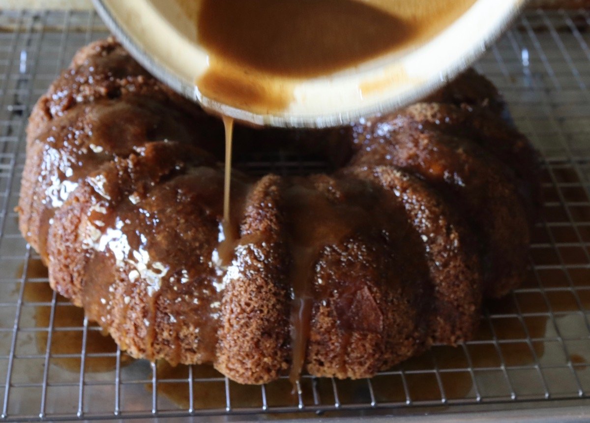 Chai glaze being drizzled over chai bundt cake on a baking rack.