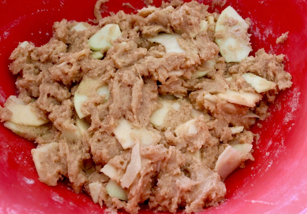 Chai cake batter full of apple slices in a red bowl.