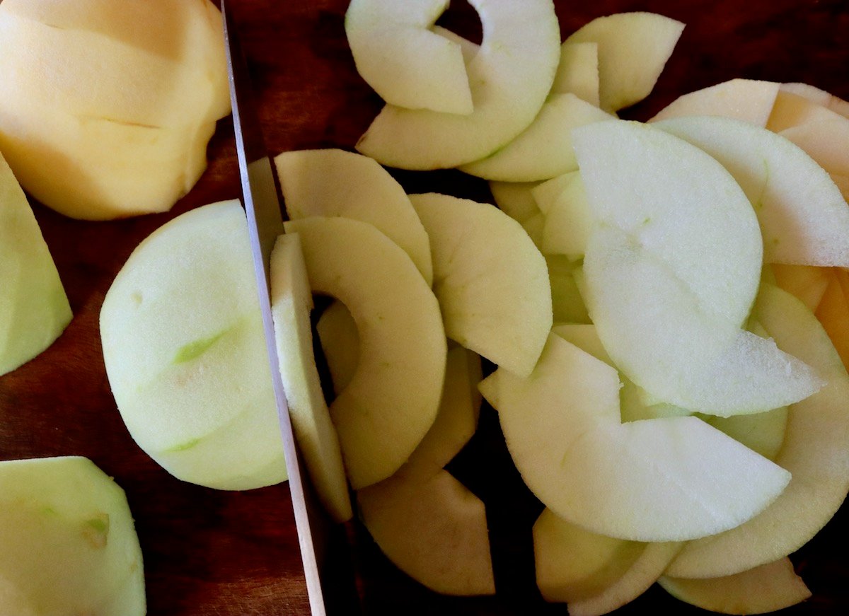 Halved and peeled apples being cut into thin slices.