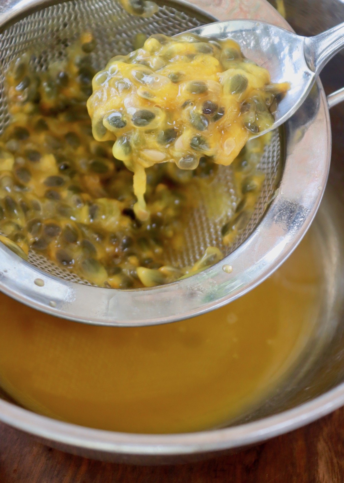 Passion fruit pulp with seeds in strainer over bowl of its juice.