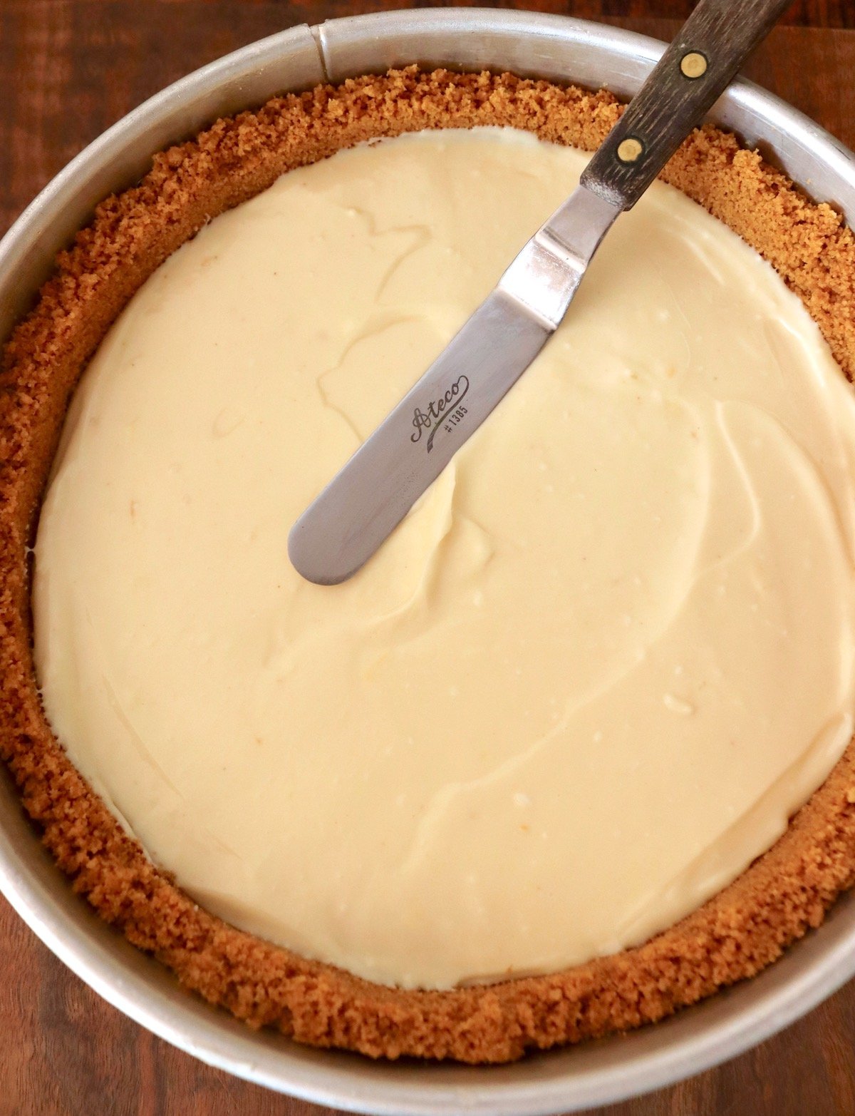 Top view of cheesecake with filling being spread smooth with small metal spatula.