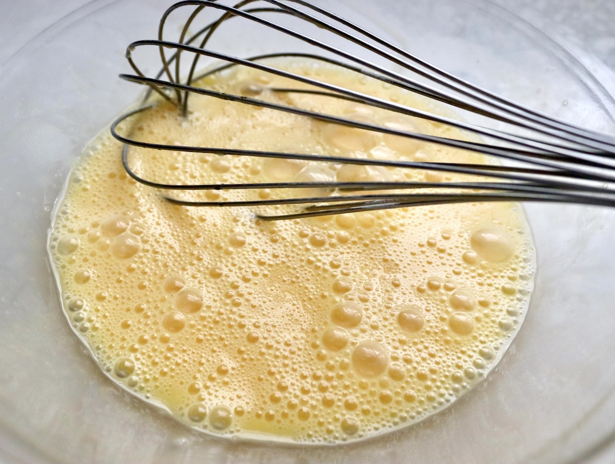 Blended eggs with a whisk in a mixing bowl.