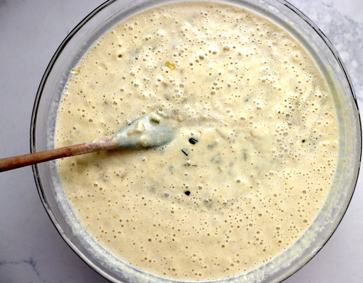 Jalapeno bacon cornbread batter mixed together in a glass bowl with a wooden spoon.