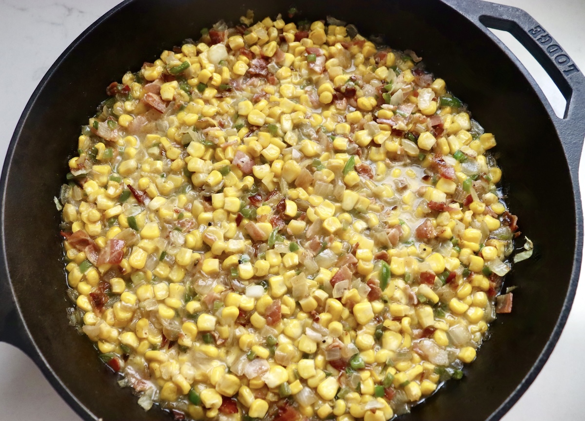 Diced onion, jalapeno, corn kernels and crumbled bacon in a cast iron skillet, mixed together with melted butter.