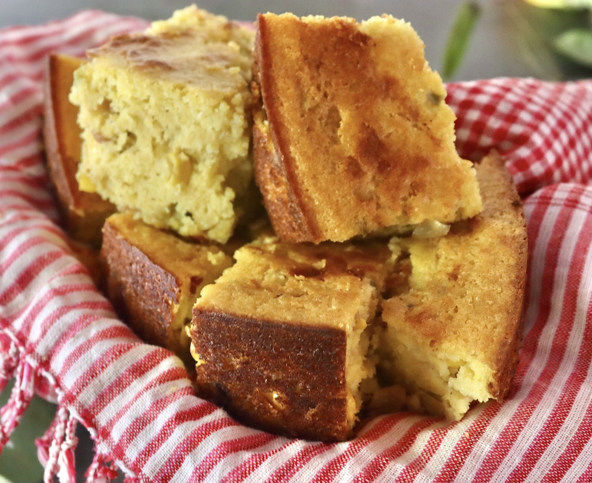 Pile of square cut cornbread with jalapeno and bacon, on a red and white cloth napkin.