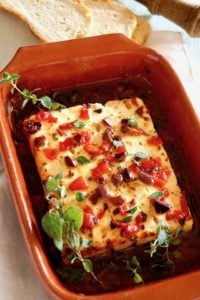 Baked Feta with Olives and Roasted Peppers with fresh oregano in a terra cotta dish