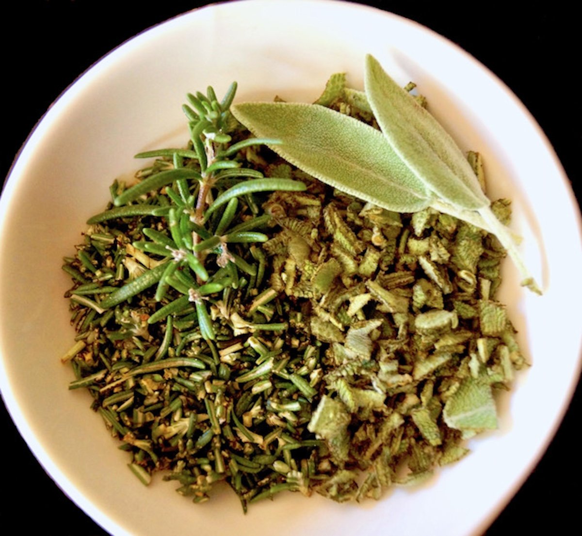 White bowl of finely chopped rosemary and sage.