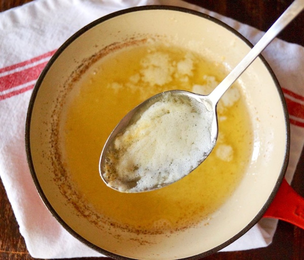 Melted butter with spoon holding up milk solids above it.