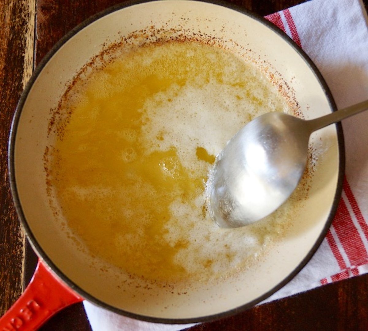 Big spoon removing milk solids from butter in small saute pan.