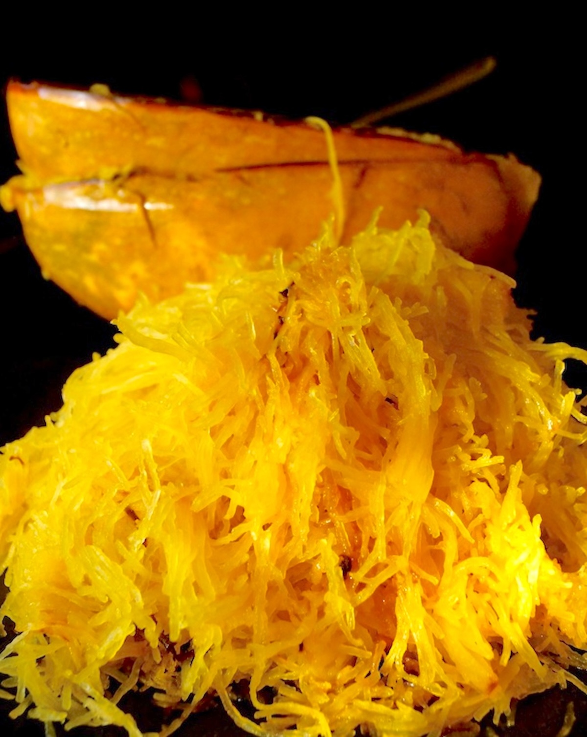 Two emptied spaghetti squash halves with the spaghetti squash piled in front of it.