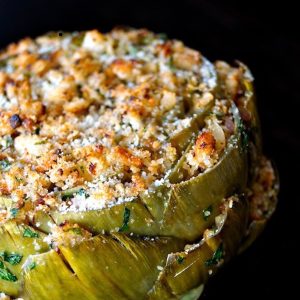 Very big stuffed artichoke that's golden on top, on a black background.