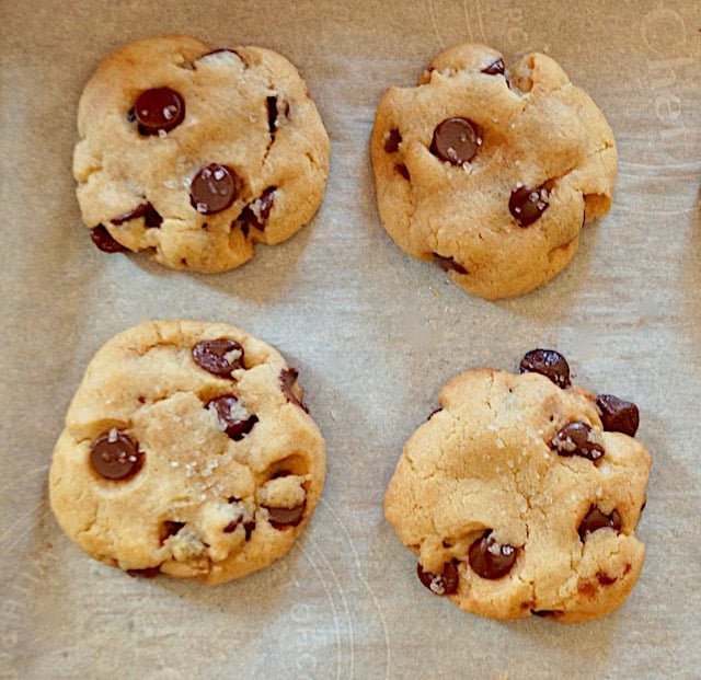 four baked olive oil chocolate chip cookies on parchment paper