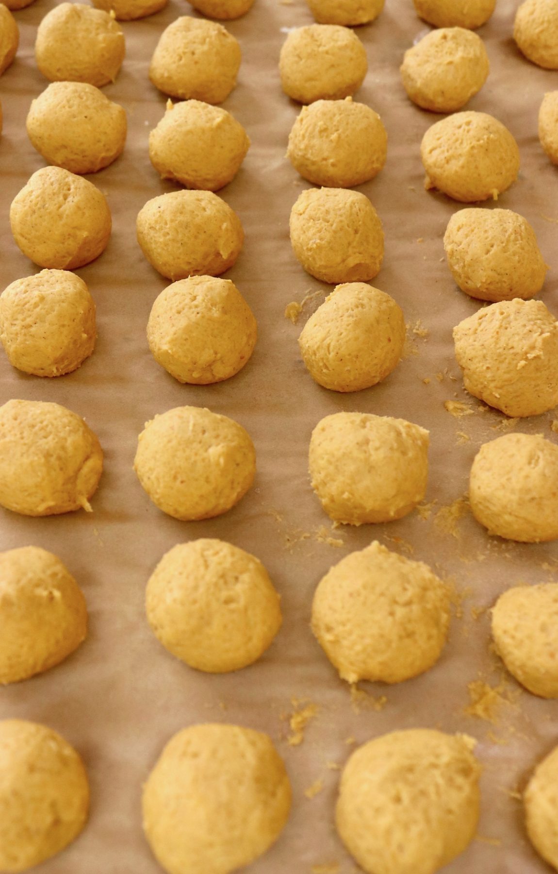 Over a dozen raw pumpkin cookie dough balls on parchment-lined baking sheet.