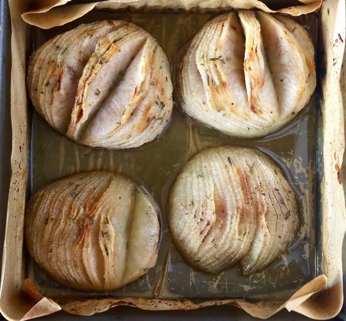 Four golden baked Asian pear halves cut with many slits that don't go all the way through.