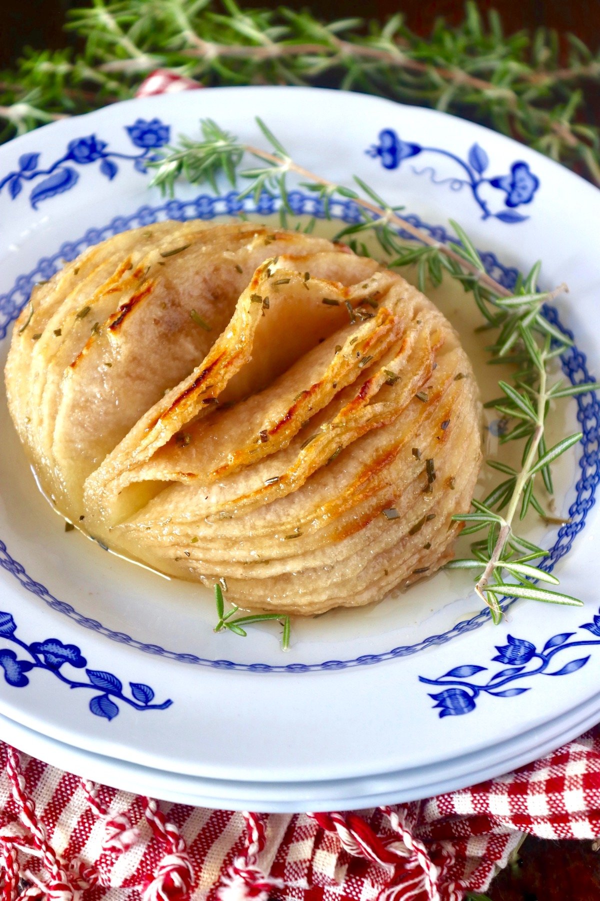 Golden roasted Hasselback Asian pear with a rosemary sprig on a blue and white plate.