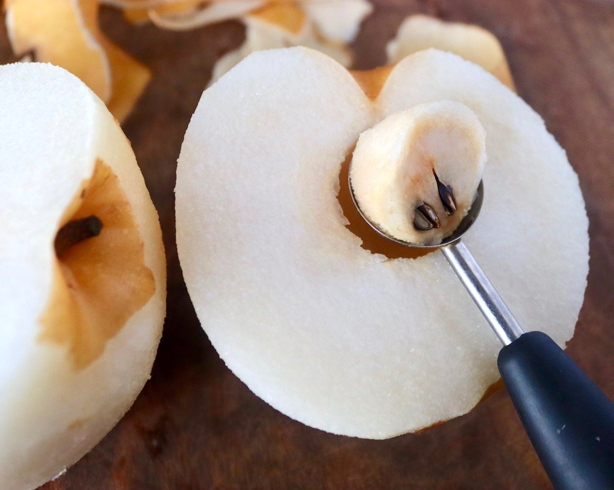 Half of an Asian pear with a melon baller scooping out the seeds.