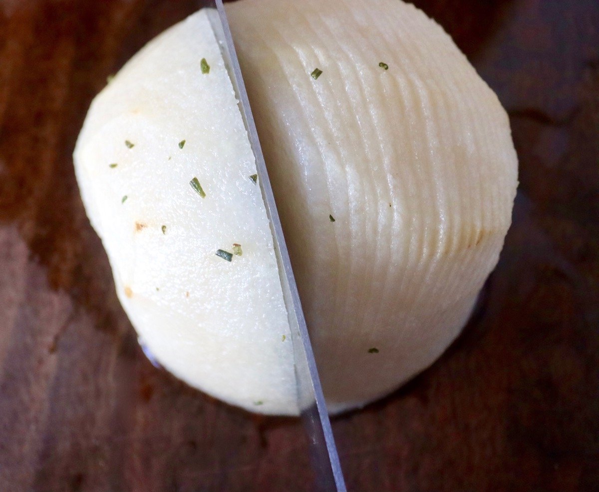 Half of an Asian pear being sliced so that it's Hasselback with many think slits that don't go all the way through.