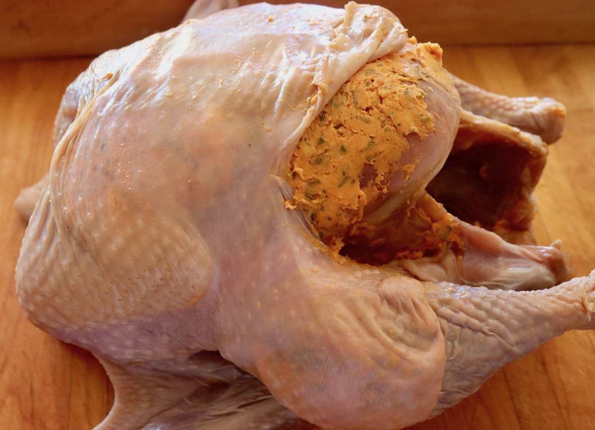 Raw, whole turkey with basting butter that's orange-colored beneath the skin.