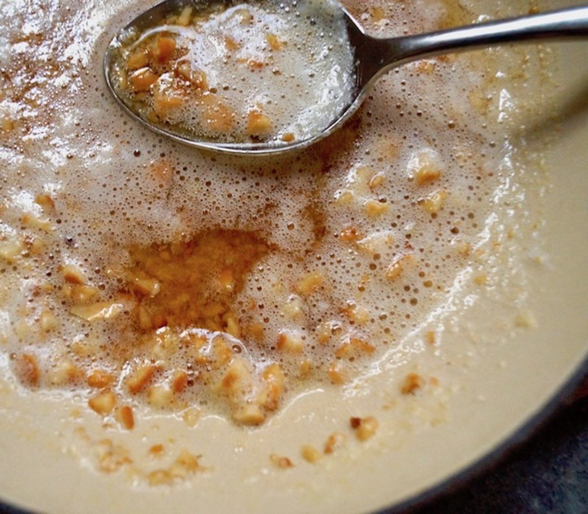 Brown butter in a saute pan with chopped hazelnuts and a spoon.