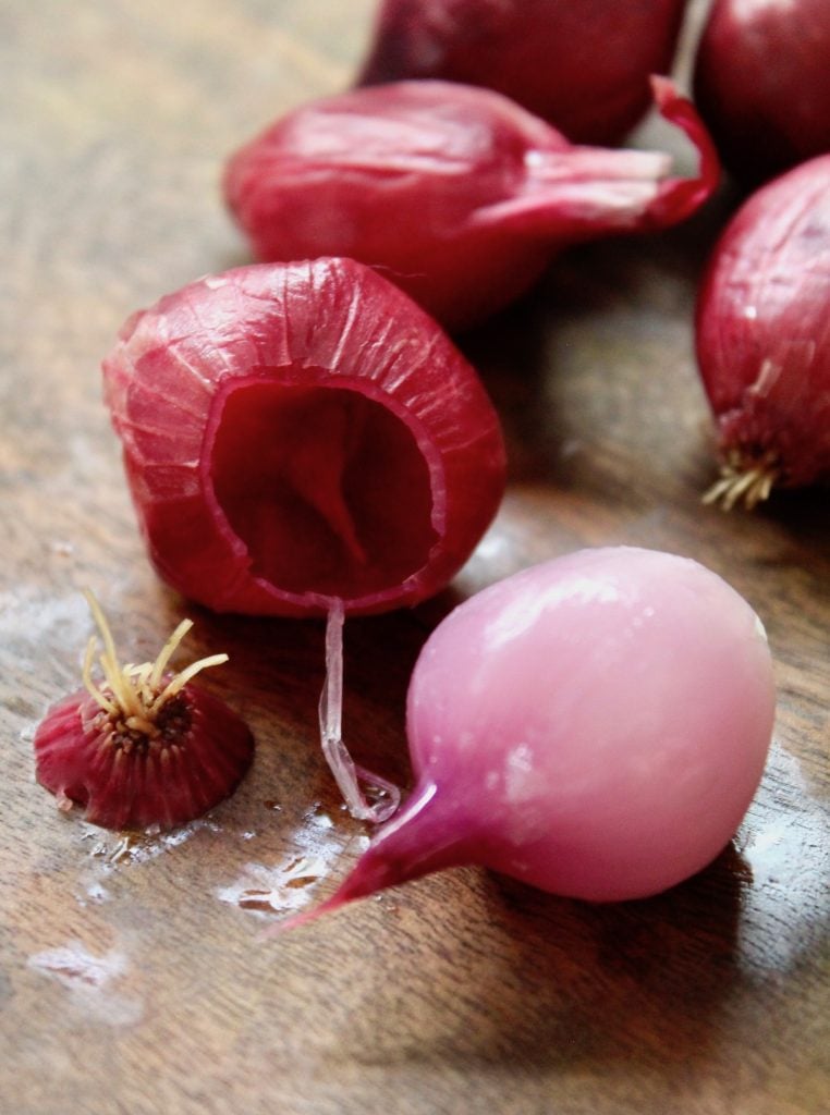How-to-Peel-Pearl-Onions one red onion that's peeledd with skin next to it on cutting board